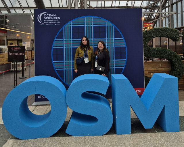 Emmanuelle et Daphée posent devant le logo de l’Ocean Sciences Meeting, représentant le Campus mondial de la mer et accueillant les participants pour présenter Sea Tech Week.